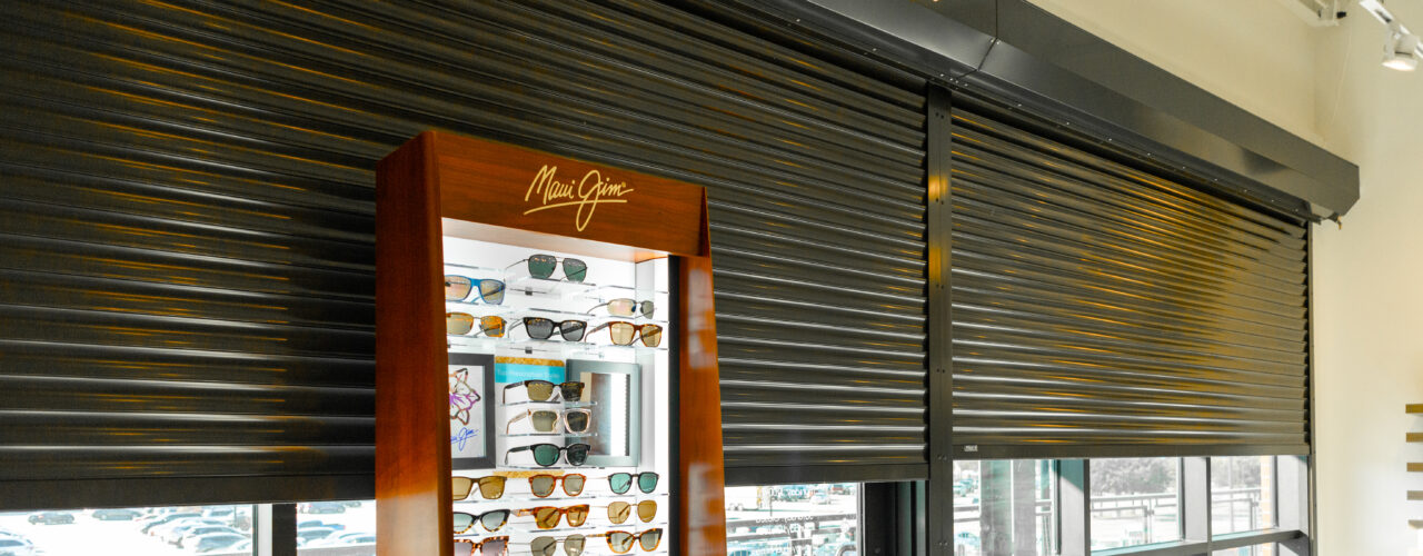 Close Up of Storefront with Security Roller Shutters Installed and a Stand of Sunglasses