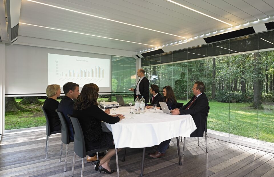office conference room meeting with presentation and windows shaded by retractable screens