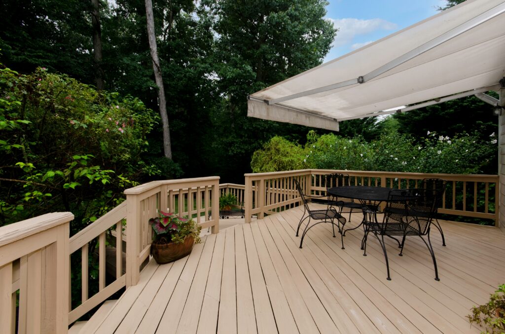 Wooden deck on back patio of home with an automated awning and patio furniture