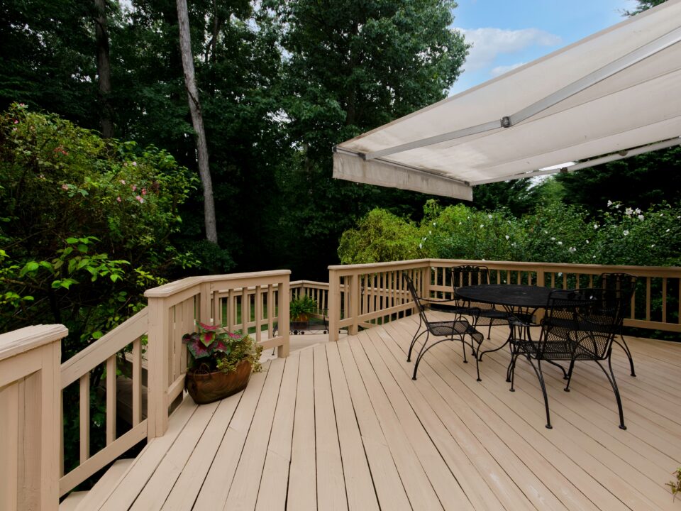 Wooden deck on back patio of home with an automated awning and patio furniture